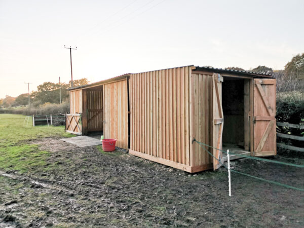 wooden horse feed store built next to large wooden barn in a field