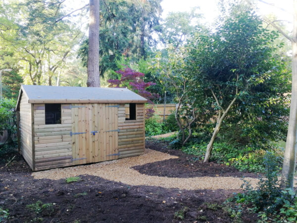 wooden shed with double doors in garden with gravel paths around it