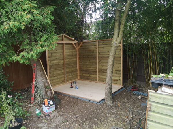 two walls of a small wood shed being built in a garden