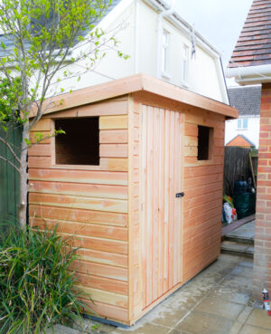 small rectangular shed for bikes down the side of a red brick house