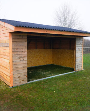 brown wood field shelter for horses with a corrugated black roof no doors standing in a field