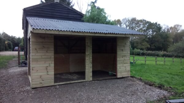 double fronted timber field shelter with a Onduline corrugated roof that looks black. It backs onto a black wooden stable