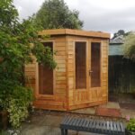 new timber summer house with glass double doors and one long window showing front and side only in garden