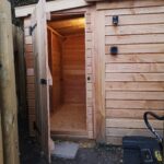 a brand new timber shed rightup against a wooden fence on the right with the door open showing the lights on inside