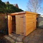 rectangle timber shed newly built with double doors one of them is open showing the light up inside