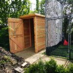 open doored brand new timber long thin shed built behind cricket nets with pent roof